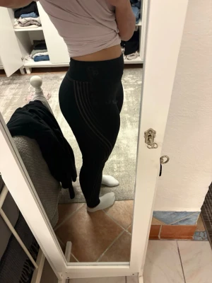 Svarta träningstights med ränder  - Säljer ett par svarta tights från  med diskreta svarta ränder längs sidorna son har börjat cracka lite. De har hög midja och sitter tight, perfekta för träning eller gymmet. Materialet är stretchigt och följsamt för maximal rörelsefrihet.