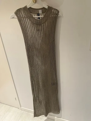 Beige stickad långklänning H&M Divided - Säljer en beige stickad långklänning från H&M Divided. Klänningen är ärmlös med grovstickat mönster och rund halsringning. Perfekt för lager på lager och ger en trendig look till sommaren.