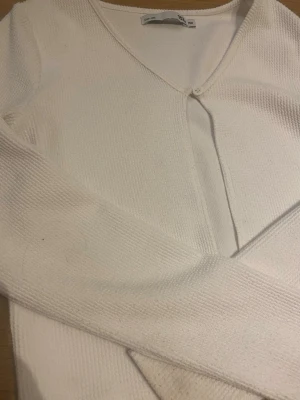 Vit ribbad kofta från 150 - Snygg vit ribbad kofta med v-ringning och knapp framtill. Långärmad modell i mjukt stickat material som passar perfekt till lager på lager. Enkel och stilren design som är lätt att matcha.