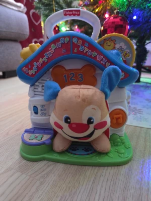 Fisher-Price interaktivt lekhus - Säljer ett färgglatt interaktivt lekhus från Fisher-Price med alfabetet, siffror och musikfunktioner. Huset är vitt med blått tak och grönt golv, och kommer med en mjuk hund i beige med blå öron och röda kinder. Perfekt för lärande och lek!