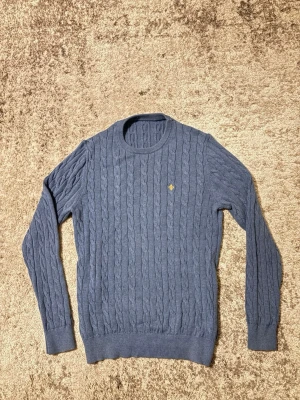 Blå kabelstickad tröja från Morris - Kabelstickad blå tröja från Morris, är tillverkad i mjukt och varmt ull som passar perfekt till höst och vinter. Storleken är M, hör gärna av dig om du har några frågor.