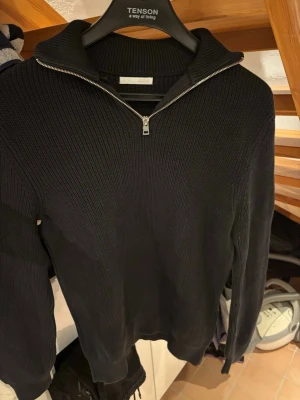 Svart stickad tröja med dragkedja (Zara, M) - Snygg svart stickad tröja från Zara med hög krage och silverfärgad dragkedja. Tröjan har ribbstickade muddar och är tillverkad i ett tjockare material.