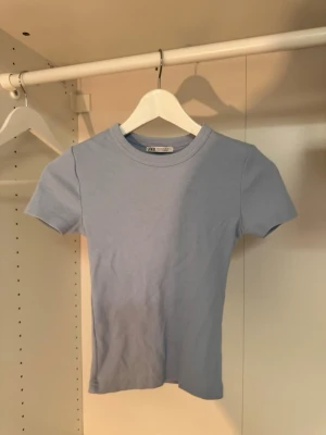 Ljusblå ribbad t-shirt från Zara - Supersnygg ljusblå ribbad t-shirt från Zara med korta ärmar och rund hals. Perfekt för en enkel och fräsch look, lätt att matcha med jeans eller kjol. Mjuk och stretchig känsla som sitter snyggt på kroppen.💙🤍