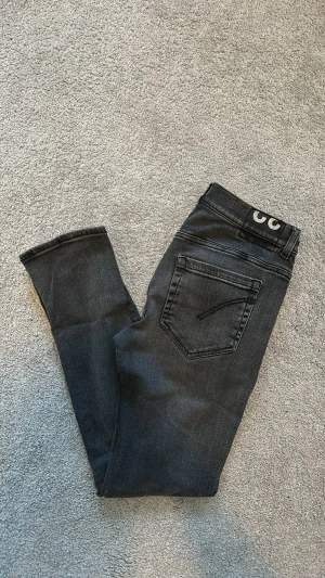 Svarta jeans från DONDUP - Snygga svarta slim fit jeans från DONDUP, modell GEORGE, med klassisk femficksdesign och diskret logga bak i midjan. Jeansen har smal passform och är tillverkade i mjukt denimtyg som sitter skönt hela dagen. Jeansen är i fint skick utan några synliga slitningar. Storlek 32. Midjemått = 40 cm. Ytterbenslängd = 101 cm. 