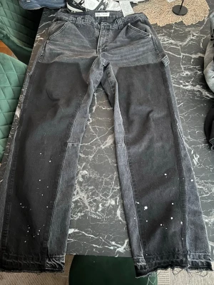 zara Flared jeans  - Unika svarta jeans från Zara med patchade detaljer och vita färgstänk på benen. Jeansen har raka ben, stora fickor både fram och bak samt en cool, lite sliten look. Perfekta för dig som vill sticka ut med en streetwear vibe.