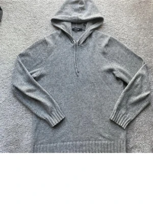 Grå stickad hoodie med huva - Mysig grå stickad hoodie med huva och dragsko. Tröjan har långa ärmar, ribbstickade muddar och bred ribbkant nedtill. Perfekt för lager-på-lager och chill dagar. Materialet ser ut att vara mjukt och värmande ullblandning.L passar M!