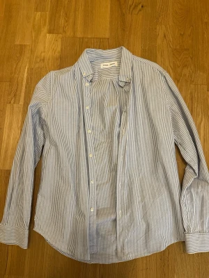 Blårandig skjorta från Samsøe Samsøe - Klassisk blårandig skjorta från Samsøe Samsøe med vit botten och smala blå ränder. Skjortan har lång ärm, knappar framtill och en avslappnad passform. Perfekt till jeans eller chinos för en clean look.
