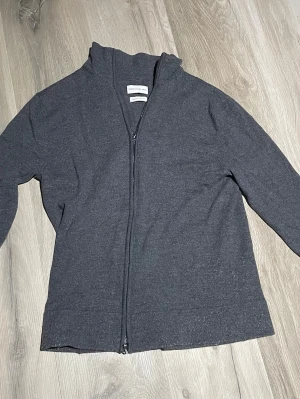 Mörkgrå ziptröja från THESE GLORY DAYS  - Mörkgrå ziptröja från THESE GLORY DAYS med hel dragkedja framtill. Tröjan är i meriono ul som är väldigt skönt och mysigt material som passar alla årstider. Storlek L men passar M