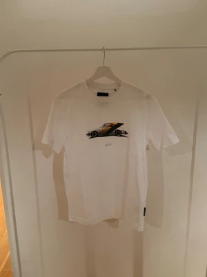 Boss x Porsche T-shirt - Stilren T-shirt från samarbetet mellan Boss x Porsche, perfekt för dig som gillar att gå med stil. Tyvärr har en liten del av texten på framsidan fallit av. (Storlek S). Köpta i en av boss butikerna i Schweiz för cirka 1700kr men vi säljer för endast 529kr!!  Slutsåld i deras butiker och online!  Rabatt för seriösa köpare!!