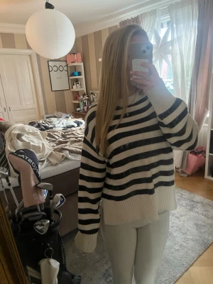 Randig stickad tröja i vitt och marinblått - Snygg stickad tröja med breda marinblåa och vita ränder. Tröjan har en avslappnad passform, långa ärmar och ribbade muddar vid ärmslut och nederkant. Perfekt för en chill och trendig look.