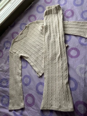  Nelly Set - Mysigt loungewear-set i beige med ribbat mönster. Setet består av en långärmad tröja med rund hals, wide arms och matchande low-waist byxor som har wideleg. Perfekt för chill dagar hemma eller när du vill vara bekvämt klädd. Materialet känns mjukt och stretchigt. Setet är helt nytt, har bara testat det och aldrig använt det efteråt.
