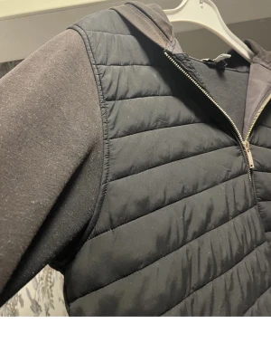 Svart cardigan  - Svart teddyjacka med quiltad framsida, huva och dragkedja. Ärmarna är i mjukt tyg och jackan har två fickor med dragkedjor. Perfekt för en chill och avslappnad stil.Jackan är köpt ifrån zalando för 2900