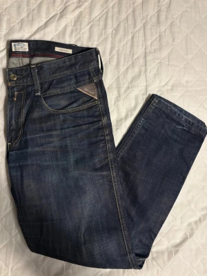 Replay Anbass - Snygga mörkblå jeans från Replay, modell Anbass. Storlek 34/32. Jeansen har detaljerade sömmar och logotyp vid fickan. Perfekta för dig som gillar stilrena och tidlösa jeans. Hör av dig vid frågor eller intresse!