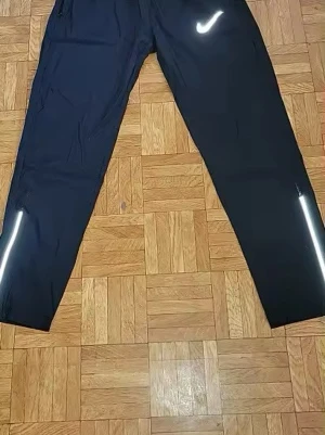Svarta träningsbyxor från Nike - Säljer ett par svarta träningsbyxor från Nike med vit logga på låret och reflekterande detaljer vid bensluten. Byxorna har rak passform och är tillverkade i ett lätt, funktionellt material som passar perfekt för löpning eller gym.