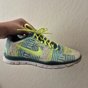 Nike sneakers med mönster och neon - Nike sneakers i storlek 40 med coolt grafiskt mönster i blått, vitt och neongult. Skorna har neongula snören och swoosh, samt vit och grön sula. Ovandelen är i syntetmaterial och mesh för bra andningsförmåga. Perfekta för dig som gillar färg och sportig stil.