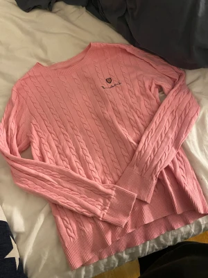 Rosa kabelstickad tröja Bondelid - Säljer en rosa kabelstickad tröja från Bondelid med rund halsringning och broderad logga på bröstet. Tröjan har långa ärmar och ribbade muddar vid ärmslut och nederkant. Perfekt för dig som gillar klassisk och stilren stickad look.