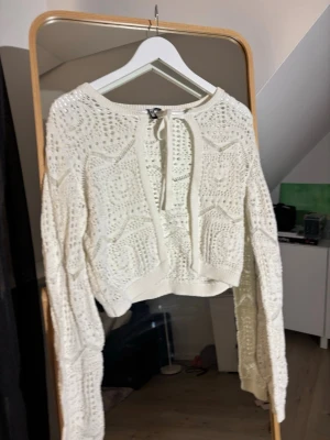 Vit virkad kofta med knytband - Säljer en söt vit virkad kofta med knytband fram. Koftan har ett luftigt mönster, långa ärmar och är något croppad i modellen. Perfekt att slänga över ett linne eller klänning för en chill look.