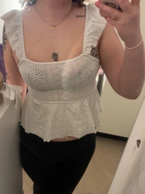 Vit topp med volang och öppen rygg - Söt vit topp med broderade detaljer, volangärmar, fyrkantig ringning och öppen rygg med knytband. Perfekt för en somrig look.