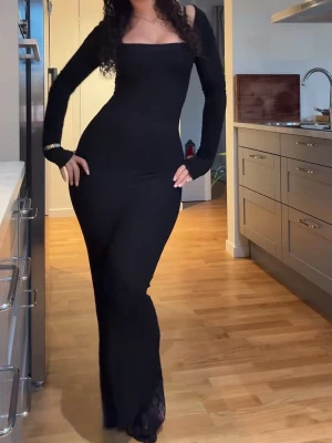 SKIMS Svart långärmad långklänning - Snygg svart långklänning ifrån SKIMS med lång ärm och fyrkantig urringning. Klänningen har en tight passform som framhäver figuren och är perfekt för dig som gillar en stilren och elegant look. Materialet är stretchigt och bekvämt.