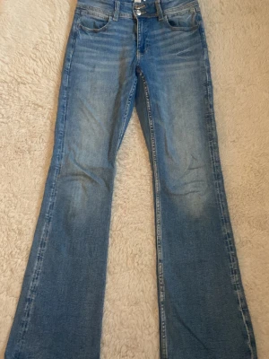 Blå bootcut jeans från gina tricot - Snygga blå bootcut jeans från gina tricot med klassisk femficksdesign och broderad bakficka. Jeansen har en ljus tvätt och är tillverkade i slitstark bomullsdenim. Perfekta för en avslappnad och trendig look.