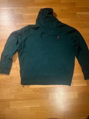 Mörkgrön tröja Polo Ralph Lauren XL - Mörkgrön långärmad tröja från Polo Ralph Lauren i storlek XL. Tröjan har hög krage med två knappar och den klassiska röda loggan broderad på bröstet. Tillverkad i mjuk bomull och polyesterblandning, perfekt för kyliga dagar.
