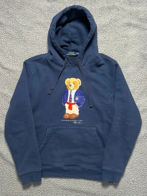 Mörkblå polo bear hoodie från polo Ralph lauren - Säljer denna snygga polo bear hoodie. Mycket bra skick, inga hål eller fläckar. Trycket är LITE skavigt. Skickar snabbt efter att du har beställt. Frågor? Skicka ett meddelande🤝