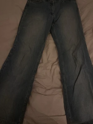 Blåa wide jeans med rak passform - Säljer ett par klassiska blåa jeans med breda ben och rak passform. Jeansen har fem fickor och subtila slitningar för en avslappnad look. Perfekta för dig som gillar en loose och bekväm stil. Materialet är tåligt denim i bomull.