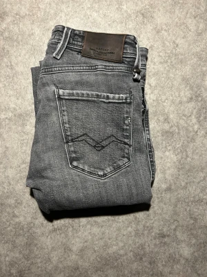Replay Jeans - Snygga grå jeans från Replay med raka ben och klassisk femficksdesign. Jeansen har diskreta slitningar och detaljer på bakfickan samt läderpatch med Replay-logga i midjan. Perfekta för en avslappnad och trendig look. W28L30