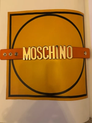 Moschino armband - Snyggt orange armband från Moschino med stora guldfärgade bokstäver som stavar ut märkesnamnet. 