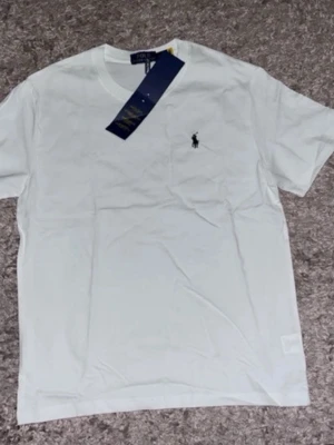 Vit t-shirt från Polo Ralph Lauren - Klassisk vit t-shirt från Polo Ralph Lauren med den ikoniska broderade loggan på bröstet. T-shirten har rund hals, korta ärmar och är gjord i mjuk bomull för en skön känsla. Perfekt basic-plagg med snygg passform.