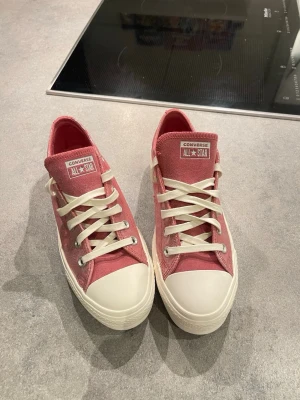 Rosa Converse All Star sneakers - Säljer ett par rosa Converse All Star sneakers med vit platt sula och snörning. Skorna har en glittrig finish och klassisk rund tå. Perfekta för dig som vill sticka ut med en cool och färgglad stil.