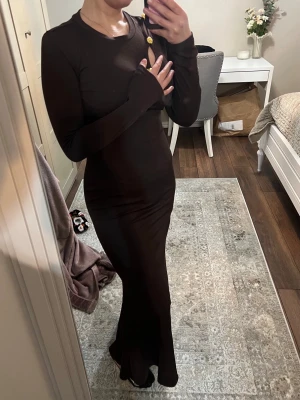 Svart långärmad långklänning - Säljer en svart, figurnära långklänning med långa ärmar och rund halsringning. Klänningen har en enkel och stilren design utan synliga detaljer eller mönster. Perfekt för dig som gillar minimalistisk stil.