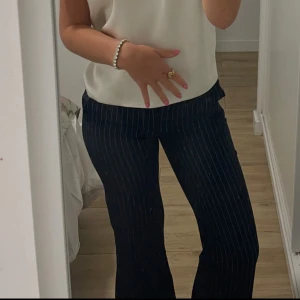 Mörkblå randiga kostymbyxor - Snygga mörkblå kostymbyxor med vita tunna ränder. Byxorna har en rak passform och klassisk midja. Perfekta för en stilren och trendig look. Materialet känns mjukt och har en lätt stretch för extra komfort.