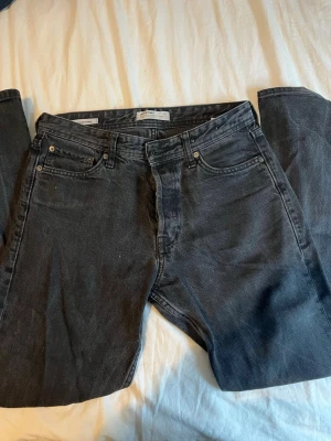 Svarta Jack & Jones jeans - Klassiska svarta Jack & Jones  jeans med rak passform och fem fickor. Jeansen har knappgylf och är tillverkade i slitstark bomullsdenim. Perfekta för dig som gillar en tidlös och clean look. Strl W 29, L 32. Modell loose/chris