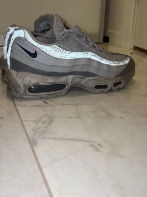 Nike Air Max 95 grå sneakers - Säljer ett par riktigt snygga Nike Air Max 95 sneakers som är perfekt för sommaren och våren. De är bekväma samtidigt som de är väldigt snygga. Som man ser på en av bilderna har en bit av det ena snörets sko lossnat men det påverkade inte mig mycket när jag använde de. Förutom det är skicket 6,5 av 10 skulle jag säga men med lite rengöring kan jag få upp de till 7,5 . Säljer de för att jag har växt ut ur de. Nypris runt 2200kr. Priset kan diskuteras 