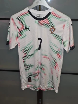 Ronaldo  - Säljer en vit Portugal matchtröja från Puma med färgstarka mönster i grönt, rött och svart. Tröjan har nummer 7 och Ronaldo på ryggen samt Portugals landslagsemblem på bröstet. Tillverkad i lätt och ventilerande material, perfekt för fotbollsträning eller match. Den är oanvänd men den är tvättad. Tveka inte för att ställa frågor! Priset är inte hugget i sten.