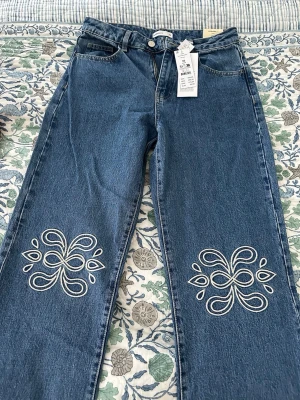 Jeans från ginatricot - Jeans med hög midja och broderier på framsidan av benen i storlek 36. Helt nya med prislapp på.