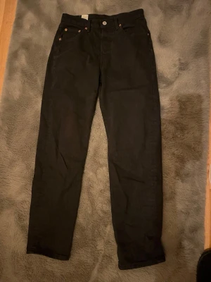 Svarta Levi's 501 jeans straight fit - Klassiska svarta Levi's 501 jeans med rak passform och fem fickor. Jeansen är tillverkade i slitstarkt bomullsdenim. Perfekta för dig som gillar tidlös stil och vill ha ett par jeans som funkar till allt.