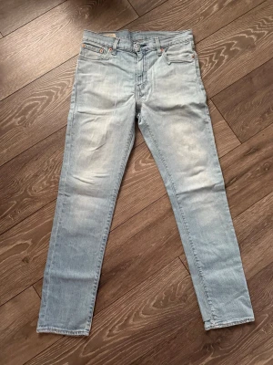 Levi's 511 ljusblå jeans - Säljer ett par ljusblå Levi's 511 jeans med klassisk femficksdesign och läderpatch bak i midjan. Jeansen har en slim passform och raka ben, tillverkade i mjuk bomullsdenim. Perfekta för dig som gillar en clean och enkel look. De är lite smutsiga där bak som man ser på sista bilden, därav priset, fri frakt