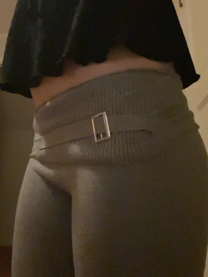 Grå mjukisbyxor med bältesdetalj - Snygga grå mjukisbyxor med bred ribbad midja och dekorativt bälte med silverfärgat spänne.Jag har bara använt dessa ett fåtal gånger så de är i bra skick! Det står att dessa är i medium men jag skulle nog säga närmre Xs/s.