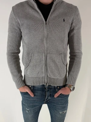 Grå ziptröja från Ralph Lauren - Säljer en riktigt snygg grå ziptröja från Ralph Lauren med ribbade muddar, två framfickor och liten broderad logga på bröstet. Riktigt snygg, men säljer pga lite för liten. Storleken är 14-16år, men skulle säga att den sitter som en XS ungefär. Jag är 174cm lång och väger 62kg. 