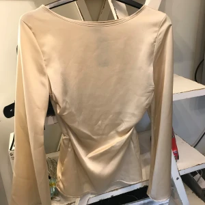  blus från Boohoo - Snygg champagnefärgad blus från Boohoo med rund halsringning och markerad midja. Blusen har långa vida ärmar och ett satinliknande tyg. Perfekt för dig som vill ha en stilren och elegant topp. Aldrig använd!