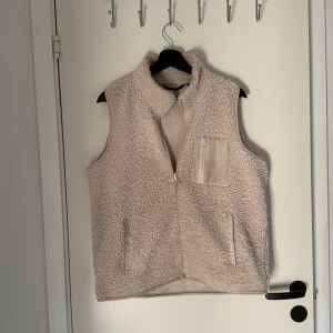 Teddyväst  - Mysig teddyväst från Vero Moda med lite högre krage och dragkedja framtill. Västen har en bröstficka med dragkedja och två sidofickor. Perfekt att slänga över en hoodie eller tröja för extra värme under kyliga dagar. Använd, men i väldigt gott skick, passar perfekt nu i början av hösten men även våren och en del av sommaren med!🤩Beige/Creme White 
