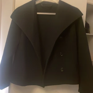 Mörkblå kappa med bred krage - Säljer en mörkblå kappa  med bred krage och tre knappar framtill. Jackan har en stilren och rak passform, långärmad design och materialet är ganska tunt som passar perfekt på sommaren