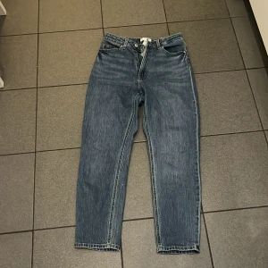 Blå raka jeans från H&M, storlek 36 - Klassiska blå jeans från H&M i rak modell med hög midja. Jeansen har fem fickor, bälteshällor och stängs med knapp och dragkedja. Tillverkade i bomull med en snygg tvättad finish och kontrastsömmar. 