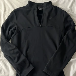 Svart half zip tröja från Energetics - Svart långärmad tröja från Energetics i storlek M. Tröjan har en praktisk half zip framtill och är gjord i mjukt, varmt syntetmaterial. Perfekt för träning eller chill dagar. Diskret logga på bröstet och enkel design utan mönster.