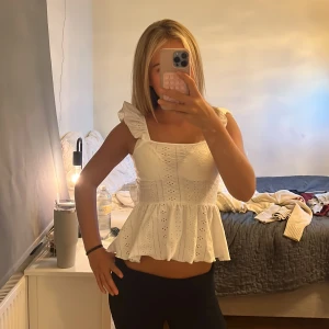 Vit volangblus med öppen rygg från SHEIN - Superfin vit blus från SHEIN i storlek XS. Toppen har volangdetaljer på axelbanden, broderade hålmönster och en peplum-nederdel. Öppen rygg med knytband ger en extra snygg touch. Perfekt för sommarens alla tillfällen!