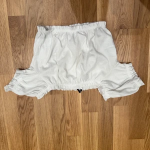 Vit offshoulder topp från H&M Divided - Säljer en söt vit offshoulder topp från H&M Divided i storlek XS. Toppen har volangiga ärmar och resår både upptill och nedtill för en snygg passform. Perfekt till sommaren och enkel att matcha med jeans eller kjol.