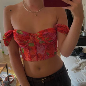Blommig rosa/röd korsettopp från Zara - Supersnygg korsettopp från Zara i mesh med blommigt mönster i rött, rosa och grönt. Offshoulder-modell med avslappnade armar och markerade kupor. Croppad passform som ger en trendig vibe, perfekt till höga jeans eller sommarkjol. Lite mindre i storlek så sitter mer som xs.