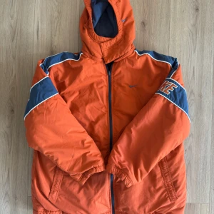 Nike orange och blå vändbar jacka 90’s vintage - Nike vändbar jacka med ena sidan i orange och blått med stora loggor och huva, och andra sidan i mjuk blå fleece med orange detaljer. Jackan har dragkedja, fickor och sportig look. Perfekt för dig som vill sticka ut med färg och streetstyle.